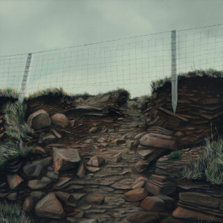 A section of fence sits on top of a rocky rise with a pale sky behind
